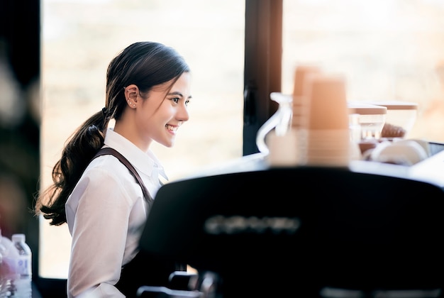 写真 ユニフォームの立って、コーヒーマシンで働く美しい女性のバリスタ。
