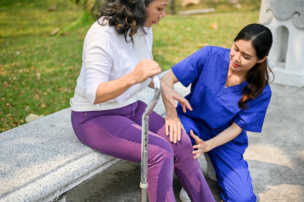 Photo beautiful female caregiver is helping and massaging an old lady's leg while resting on a bench