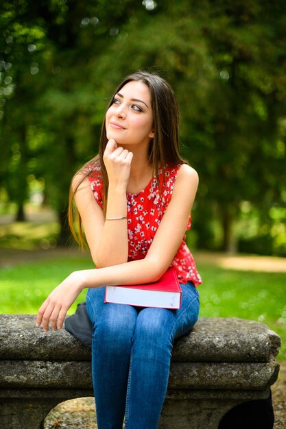 Beautiful female college student reading a book on a bench in a park