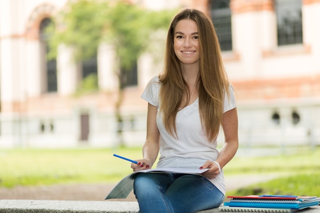 Beautiful female college student reading a book on a bench in a park