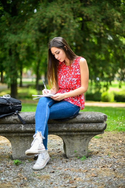 Красивая студентка колледжа, читающая книгу на скамейке в парке