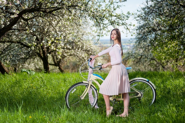 春の庭でレトロな自転車を持つ美しい女性サイクリスト