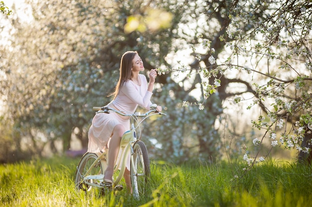 Beautiful female cyclist with retro bicycle in the spring garden