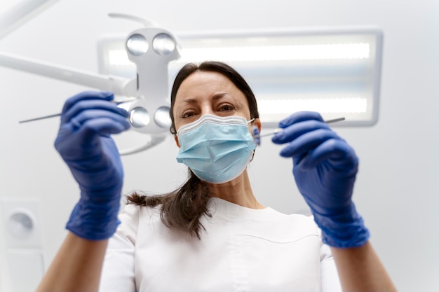 Beautiful female dentist in a protective mask holds dental instruments in her hands treats her patient's teeth Professional work of a dentist in a dental clinic