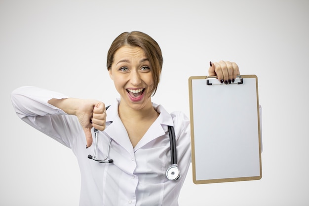 Beautiful female doctor broadly smiling showing dislike sign and blank clipboard