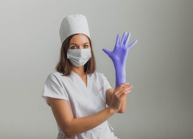 A beautiful female doctor or nurse in a protective mask and rubber gloves on a light background with copyspace. Healthcare concept