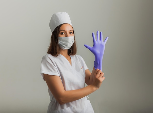 A beautiful female doctor or nurse in a protective mask and rubber gloves on a light background with copyspace. Healthcare concept