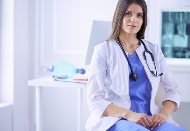 Beautiful female doctor sitting at her working place in a consulting room smiling at the camera