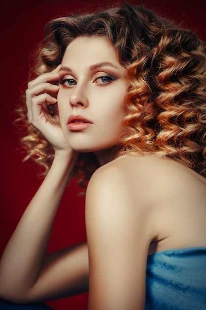 自然な完璧な肌を持つ美しい女性の顔。赤い背景に発展する美しい長い生姜髪の青いトップで美しい少女。