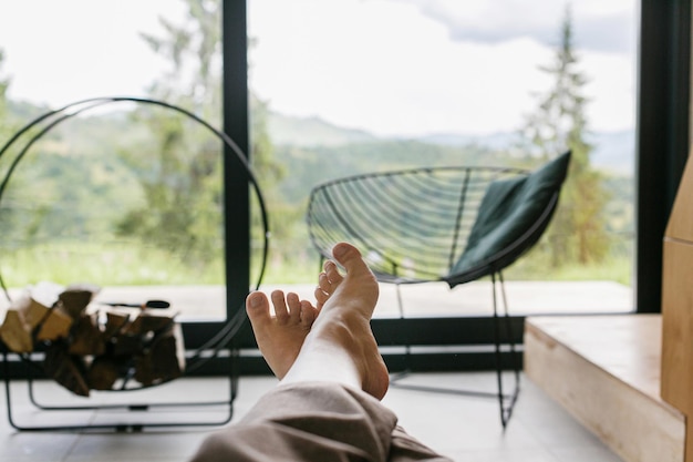 Beautiful female feet on background of firewood and big window
in modern chalet woman relaxing