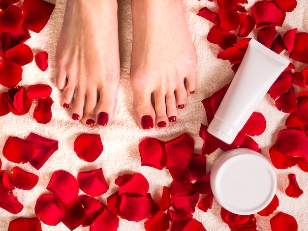 Beautiful female feet on terry towel with rose petals. jar and tube of skin care cream. spa and skin care concept