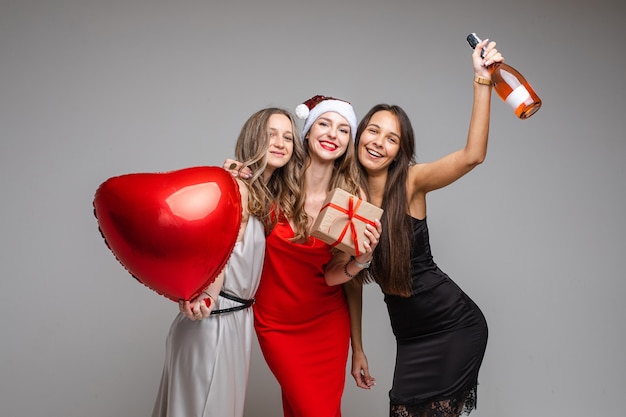 Beautiful female friends in dresses with a present, isolated on white wall