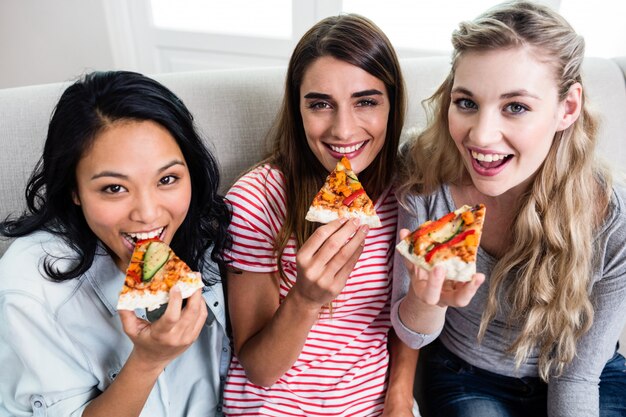 Beautiful female friends eating pizza at home