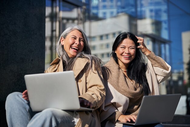 Beautiful female friends using laptops and laughing