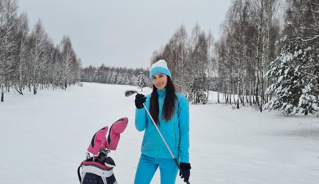 Beautiful female golfer holds a golf club in winter on golf course