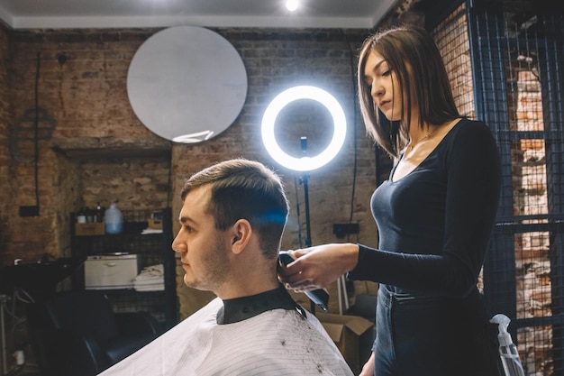 Beautiful female hairdresser cutting clients hair with scissors in a barber shop