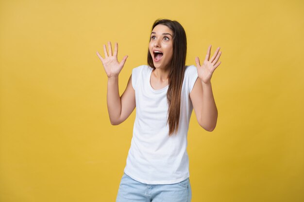 Beautiful female half-length portrait isolated on yellow studio backgroud. The young emotional smiling and surprised woman standing and looking at camera.The human emotions, facial expression concept.