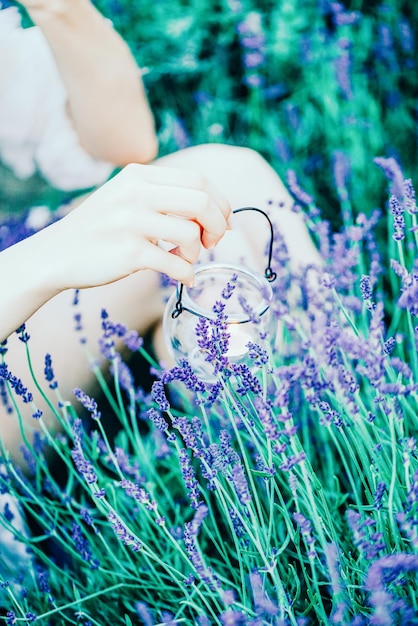 Foto una bella mano femminile che tiene un portacandele trasparente sul campo di lavanda