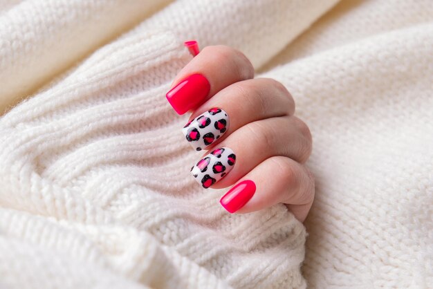 Photo beautiful female hand with pink manicure nails leopard print design on wool sweater background