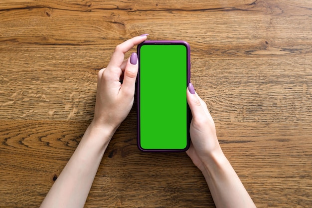 Photo beautiful female hands hold smartphone on wooden background empty green screen for picture or text