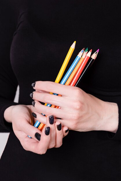 Belle mani femminili che tengono le matite colorate sul nero