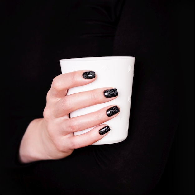 Beautiful female hands holding white cup manicure with black nail polish copy space