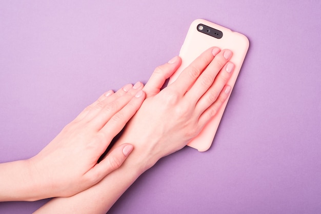 Beautiful female hands showing fresh cute manicure and holding smartphone, skin and nail care concept, purple surface