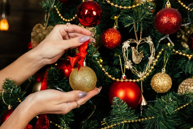 Beautiful female hands take a golden Christmas ball on a Christmas tree closeup Christmas decorations