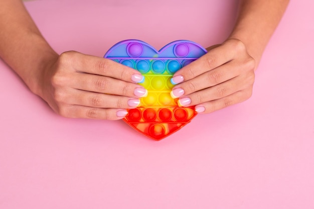 Beautiful female hands with colourful manicure nails holding toy pop it