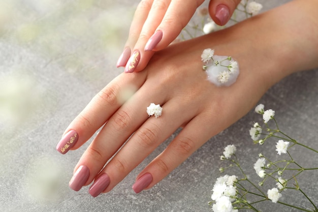 Beautiful female hands with cream on gray textured background