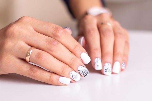 Beautiful female hands with fashion manicure nails, white and silver gel polish, stars design