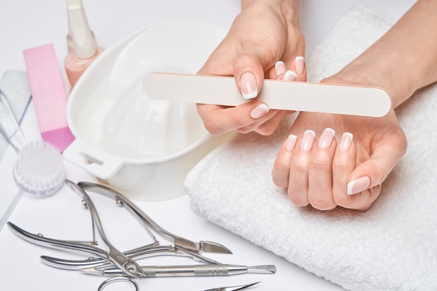 Beautiful Female Hands with French manicure over light grey background.