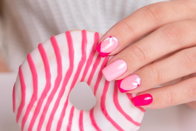 Beautiful female hands with pink manicure nails, flowers design, holding donut