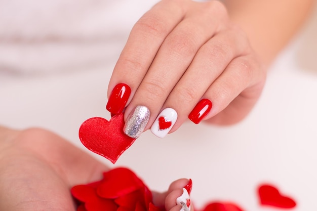 Beautiful female hands with red manicure nails hearts design on white background