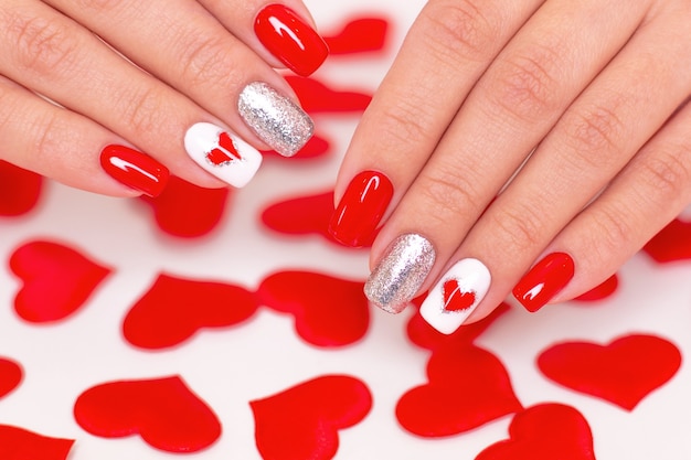 Beautiful female hands with red manicure nails, hearts and Valentine's day design