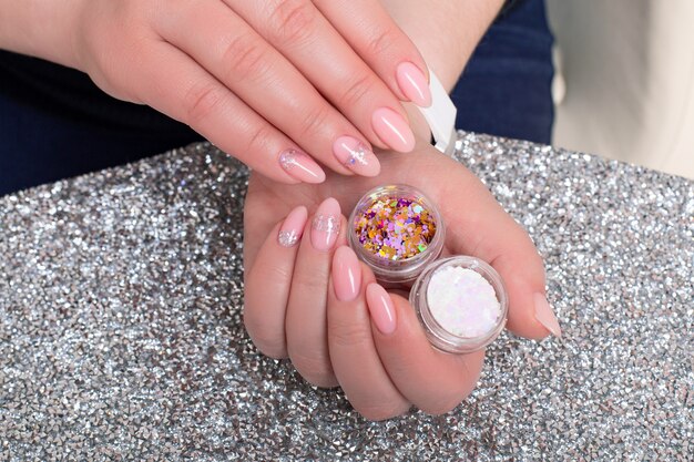 Beautiful female hands with romantic manicure nails nude gel polish with silver glitter