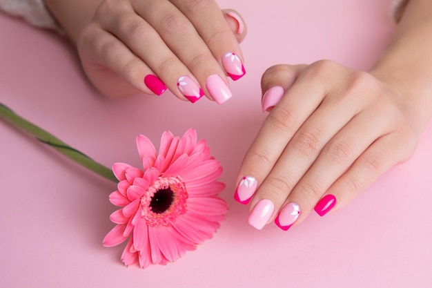 Beautiful female hands with romantic manicure nails pink gel\
polish gerbera flowers design
