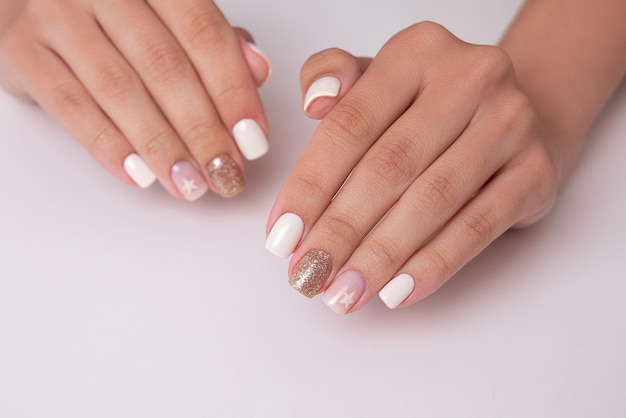 Beautiful female hands with romantic manicure nails, white gel polish with golden glitter