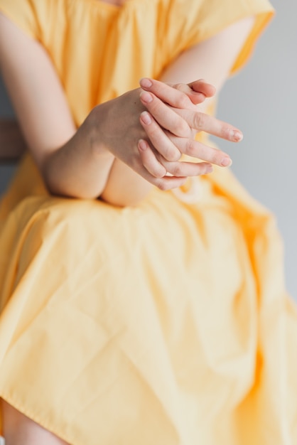 黄色の背景に美しい女性の手。あなたの手の世話をします。自然なマニキュア、清潔な肌の繊細な手のひら。淡いピンクの爪