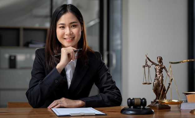 Beautiful female lawyer in suit sitting at workspace with gavel and Statue of lady justice on the table