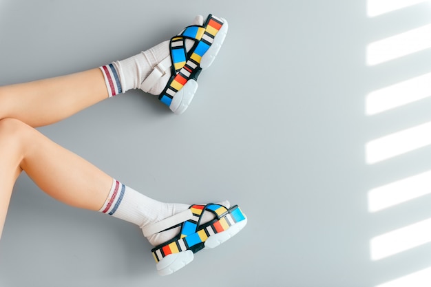 Beautiful female legs in white trendy socks posing in colorful fashionable high wedge leather sandals