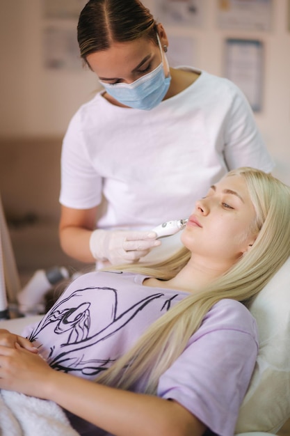 Beautiful female patient is getting a face skin treatment while lying at medical clinic