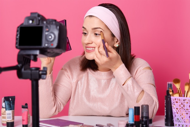 Beautiful female records video. Yong blogger shows how to apply eyeshadow. Lady advetises cosmetics on her channel