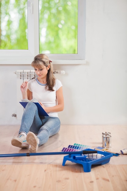 Beautiful female sitting on floor loking in clipboard and thinking