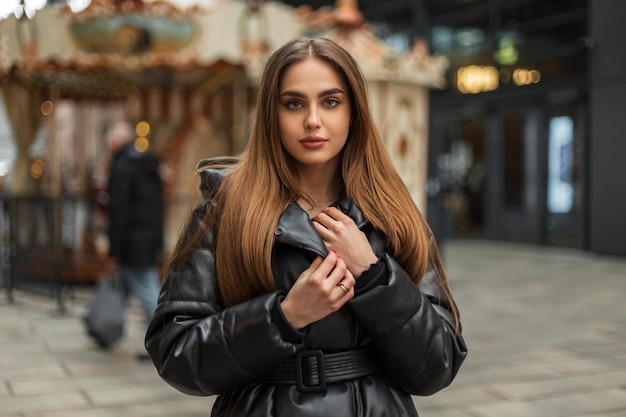 Beautiful female street portrait of a pretty caucasian woman model with green eyes in a winter fashionable black down jacket walking in a vintage park in the city