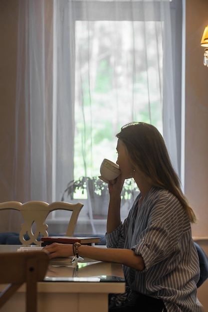 Beautiful female student drinking coffee in the cafeteria and\
reading a book during breakfast