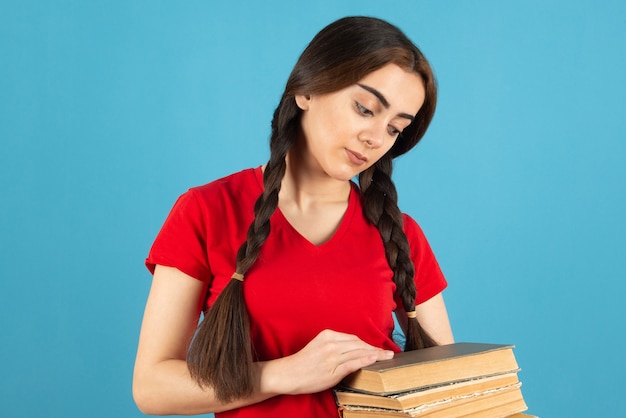 Beautiful female student in red t-shirt attentively reading book on blue wall.