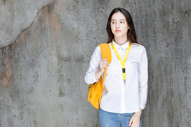 Beautiful female student with yellow backpack standing. High quality photo