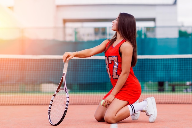 Beautiful female tennis player on tennis court in red dress