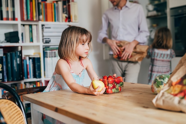 Beautiful female toddler indoor at home kitchen holding fruits